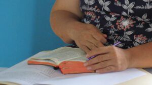 Manos sosteniendo una Biblia abierta con bordes anaranjados y un bolígrafo morado sobre documentos, 007 y la Biblia: ¿Qué revela la Sagrada Escritura sobre el famoso agente secreto?