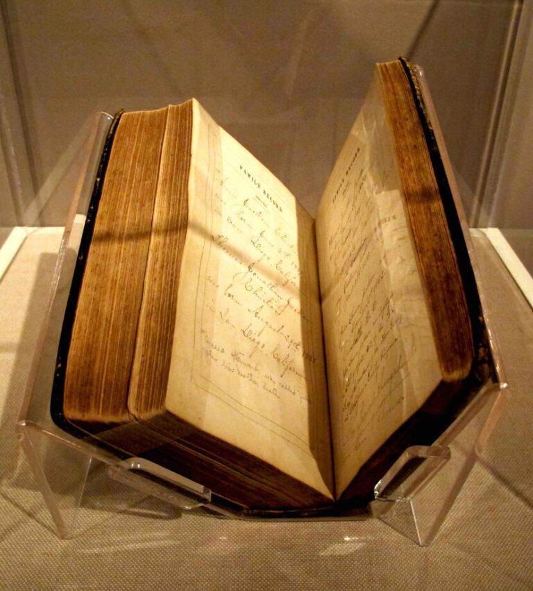 Open antique book with aged pages and handwritten notes displayed on a clear stand, The Bible: Your GPS to a Fulfilling Life.