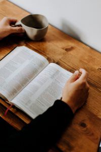 Open Bible on a wooden table with hands and a coffee mug, illustrating Why the Bible warns against trusting men: Exploring the dangers.