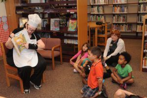 Woman in a library reading a picture book to a circle of preschool children, Teaching the Bible to 3-5 Year Olds: Tips and Tricks for Engaging Lessons.