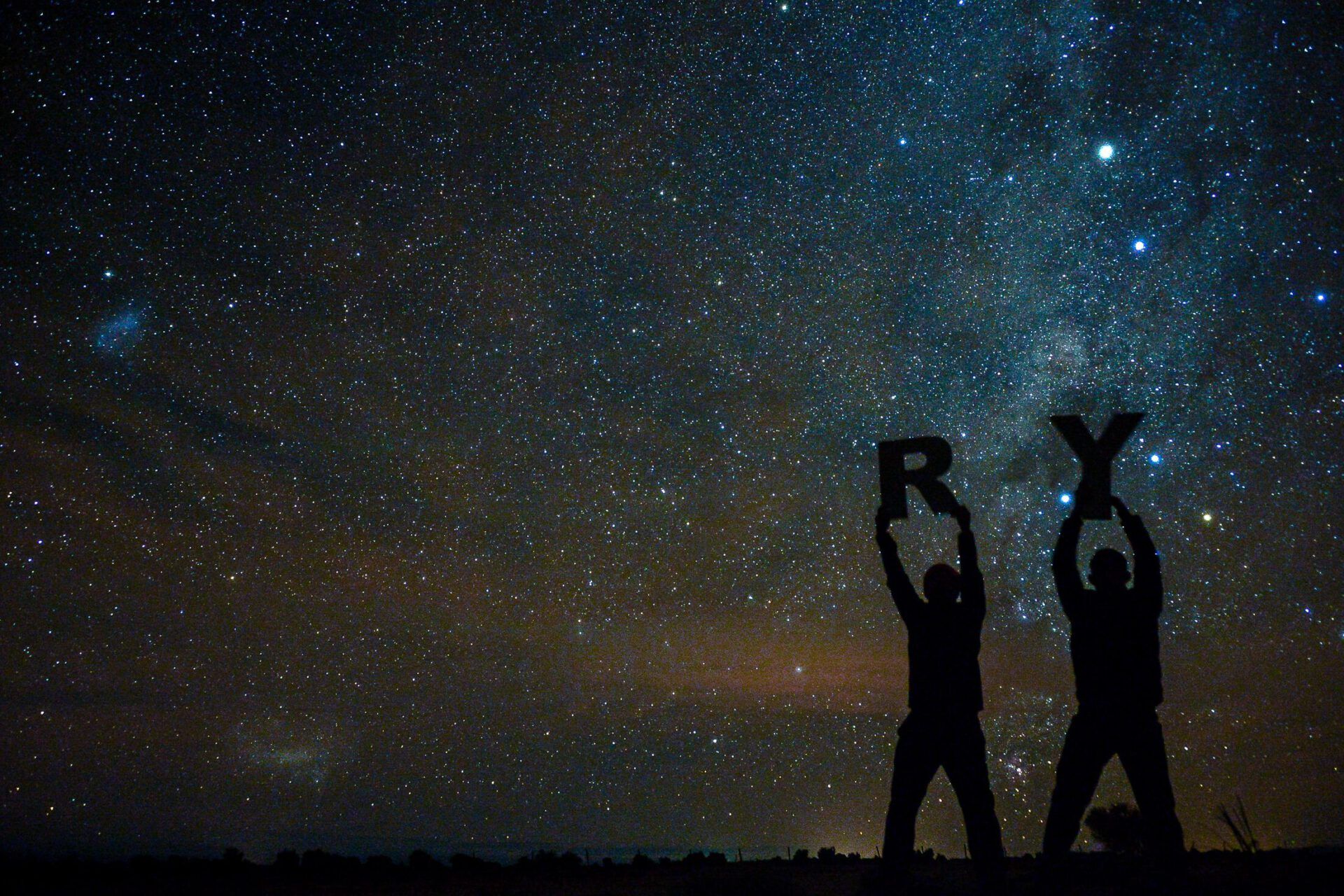 Siluetas bajo un cielo estrellado sostienen letras mientras se plantea ¿Qué dice la Biblia sobre vivir solo? Descubre las respuestas aquí