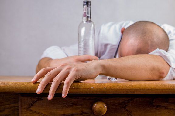 Hombre recostado sobre una mesa junto a una botella de alcohol, imagen que invita a la reflexión: ¿Qué dice la Biblia sobre los borrachos? Descubre la verdad aquí