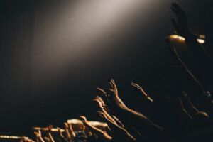 Silhouetted hands lifted in worship under a spotlight, evoking reflection on Why Skipping Church Might Not Be What the Bible Actually Says.