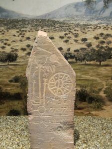 Estela de piedra tallada con petroglifos y un motivo circular tipo rueda en exposición museográfica, La historia detrás de 'cuando vinieron ellos tenían la biblia y nosotros teníamos la tierra'.
