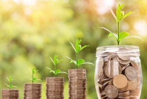 Monedas apiladas y un frasco con brotes verdes simbolizando ahorro y crecimiento, ¿Qué dice la Biblia sobre pagar deudas?