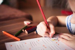 Niño escribiendo con lápiz rojo y lápices de colores sobre una hoja; ¿Qué enseña la Biblia sobre la educación de los hijos? Descubre sus consejos