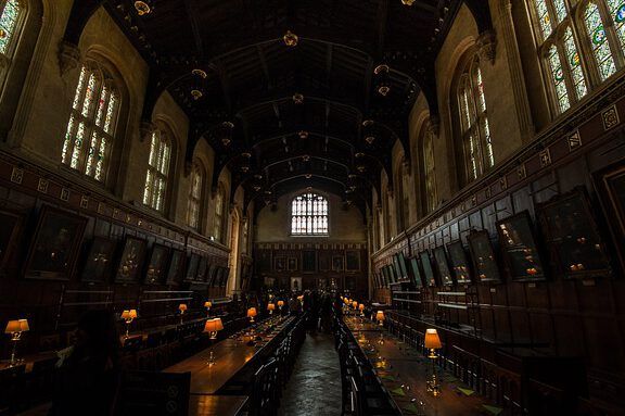 Gran salón estilo Hogwarts con largas mesas, vitrales y lámparas tenues, evocando debates culturales y preguntando ¿Es Harry Potter satánico según la Biblia?
