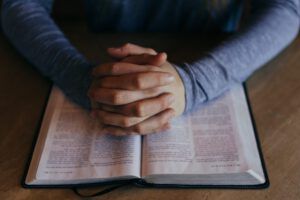 Hands folded in prayer over an open Bible illustrating Why You Should Avoid Eating Meat During Holy Week According to the Bible.