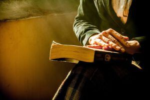 Manos descansando sobre un libro iluminado por luz cálida, ¿Qué dice la Biblia sobre el Día Internacional de la Mujer?