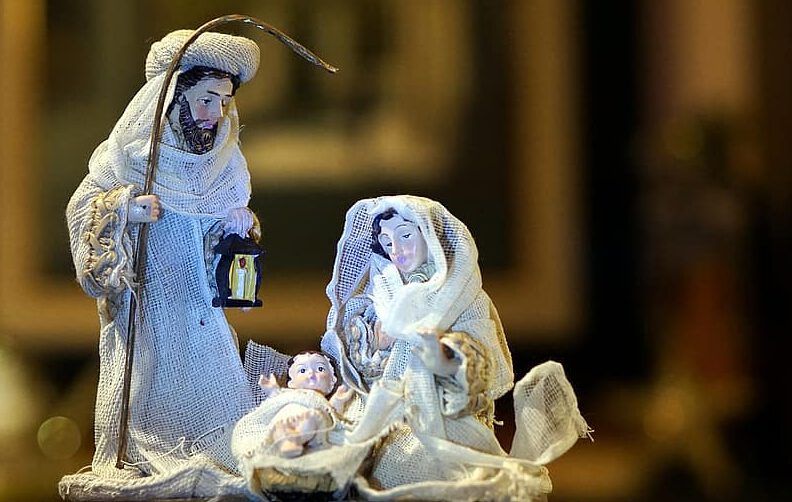 Figuras del portal de Belén con María, José y el Niño en un pesebre iluminado por una lámpara — ¿Qué dice la Biblia sobre la Navidad? Descubre la respuesta en la Reina Valera.