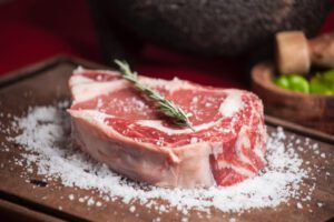 Raw marbled beef steak on a wooden board sprinkled with coarse salt and garnished with rosemary, evoking contrasts like Why Pork is Forbidden in the Bible: Surprising Revelations.