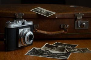 Cámara vintage junto a una maleta de cuero y fotografías en blanco y negro sobre una mesa; ¿Qué dice la Biblia sobre recordar el pasado? Descubre la respuesta aquí