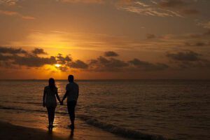Pareja caminando de la mano por la playa al atardecer, imagen para reflexión sobre Los celos en la pareja según la Biblia: ¿Qué enseña la religión de los Testigos de Jehová?