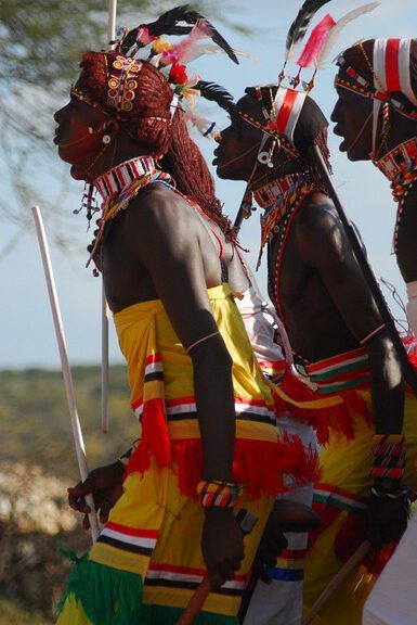 Personas en danza ceremonial con trajes tradicionales coloridos, adornos de cuentas y plumas que avanzan en fila — ¿Qué enseña la Biblia sobre el uso del rosario en la oración?