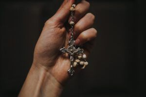 Hand holding a rosary crucifix and beads in a close-up, Why Pray the Rosary? Discover the Surprising Biblical Roots