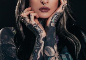 Lo que dice la Biblia sobre los tatuajes: ¿pecado o permiso divino? Mujer en primer plano con tatuajes en brazos y manos, anillos y piercing septum.