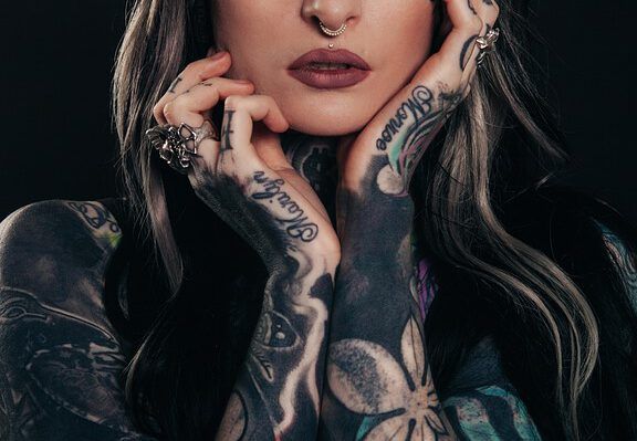Lo que dice la Biblia sobre los tatuajes: ¿pecado o permiso divino? Mujer en primer plano con tatuajes en brazos y manos, anillos y piercing septum.
