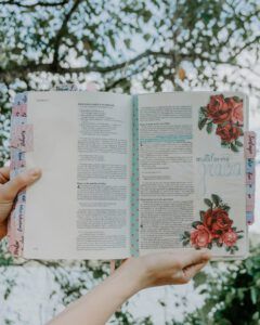 ¿Es pecado teñirse el cabello según la Biblia? Biblia abierta con anotaciones, pestañas y flores decorativas sostenida por manos al aire libre.