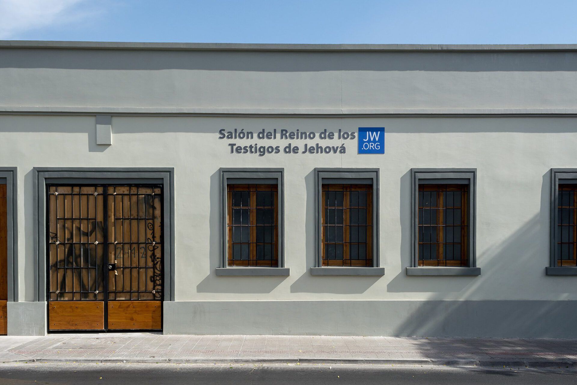 Fachada de un Salón del Reino con puerta de madera, ventanas y el letrero que invita a la pregunta ¿Qué enseña la Biblia sobre la muerte según los Testigos de Jehová?