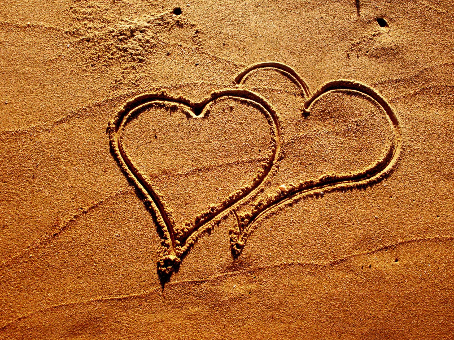 Dos corazones dibujados en la arena de la playa simbolizan amor y conexión: Lo que la Biblia revela sobre el sexo y la intimidad en pareja.