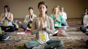 Group of people seated in a yoga meditation class with hands in prayer pose, Yoga and Sin: Uncovering the Bible's Stance.